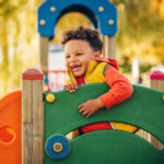 toddler boy smiling on colorful playground equipment