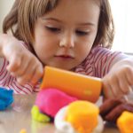 child with roller plays with dough