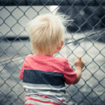 Child looking through a chain-link fence