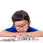 child with glasses looking at stacks of coins